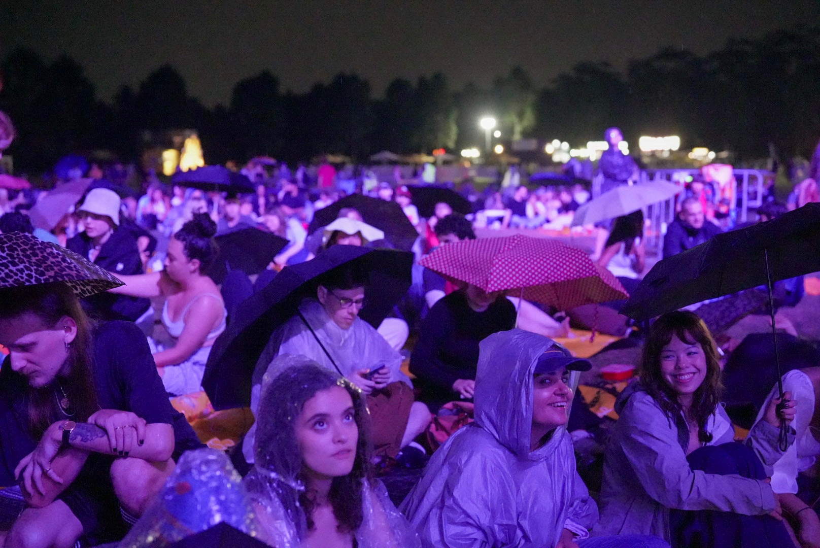 People wearing ponchos and umbrellas at an outdoor film festival.