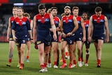 A group of Melbourne AFL players walk off the ground looking disappointed after a match at the MCG.