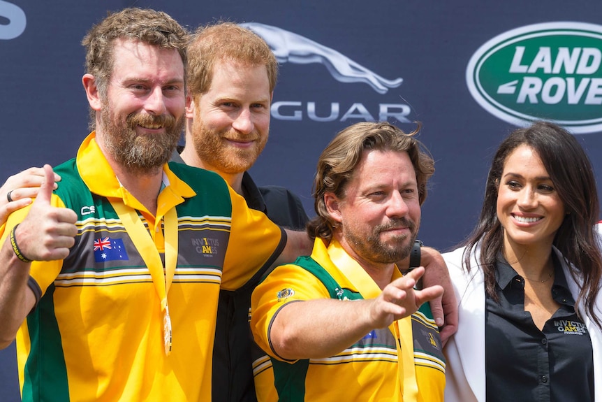 Two men in beards and Australian team uniforms stand with Prince Harry and Meghan, Duchess of Sussex.