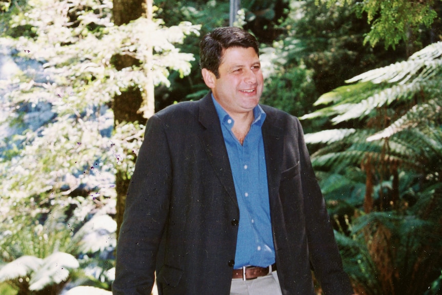 Steve Bracks poses for a photo in front of a forest and waterfall.
