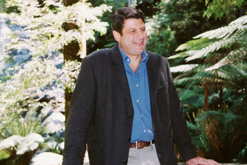 Steve Bracks poses for a photo in front of a forest and waterfall.