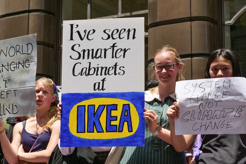 A school girl hold a sign which reads: I've seen smarter cabinets at Ikea".
