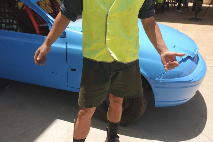 A young prisoner pictured from the neck down in front of a car