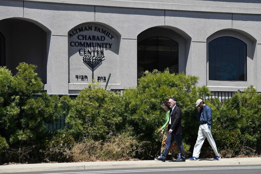 A group of people walk beside the wall of a synagogue