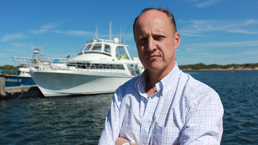 Red Rock Films president Brian Armstrong stands in front of a white boat docked in the sea.