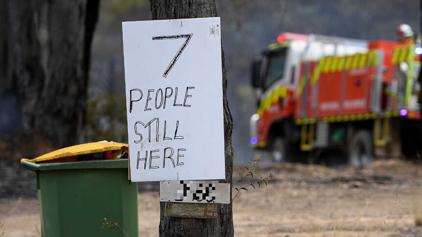 A sign stuck to a tree that reads "seven people still inside"
