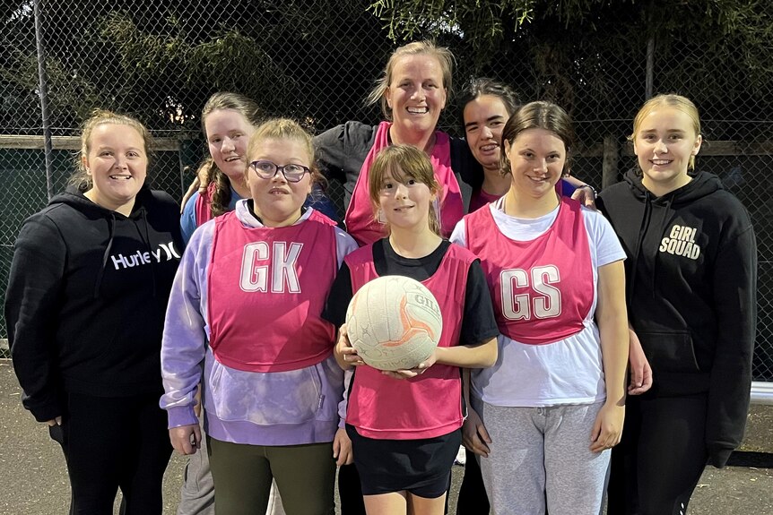 A group of girls and young women wearing netball bibs holding a ball