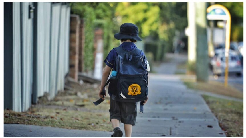 A young child in school uniform walks along a street away from the camera