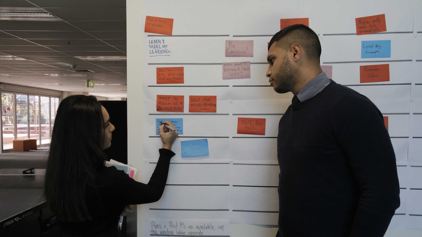 Two ABC Indigenous staff members discussing work at a white board