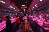 A woman wearing a hat and face masks walks down an aisle, with butcher shop meat on either side.