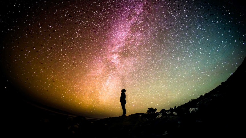 A silhouetted figure looks to the night sky, where thousands of stars are shining brightly