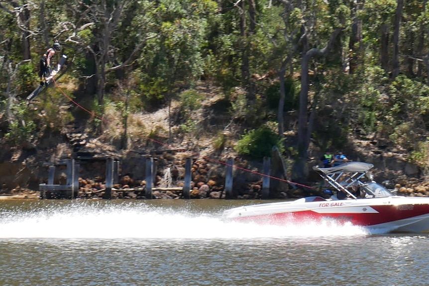 A water skier high in the air after coming off a jump towed by a boat on a river.