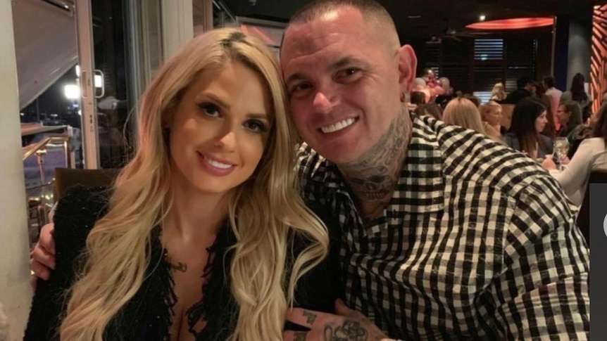 A smiling blonde woman and a heavily tattooed man, apparently at a restaurant.
