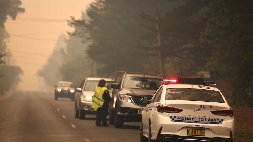A police car and a police officer talk to a driver on a smoky road
