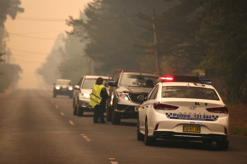 A police car and a police officer talk to a driver on a smoky road