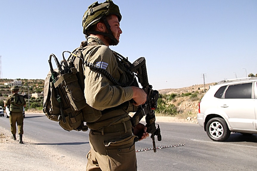 An Israeli soldier watches cars drive through a pop-up checkpoint near Beni Neiem village.