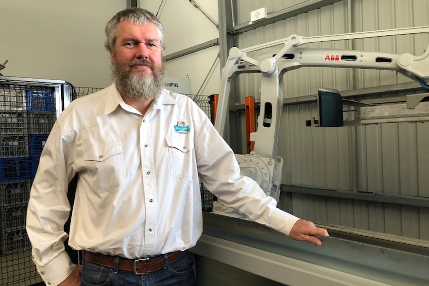 Peter Falcongreen standing in front of the robot that packs empty crates on pallets at Maleny Dairies.