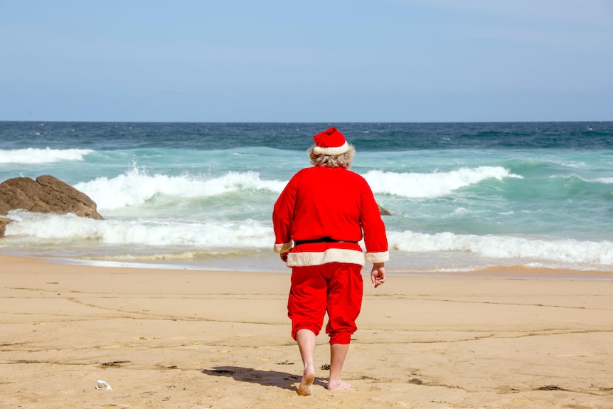 Man in red hat and suit walking towards blue water at the beach 