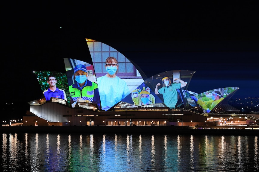 photos of nurses and healthcare workers wearing masks projected onto the opera house sails