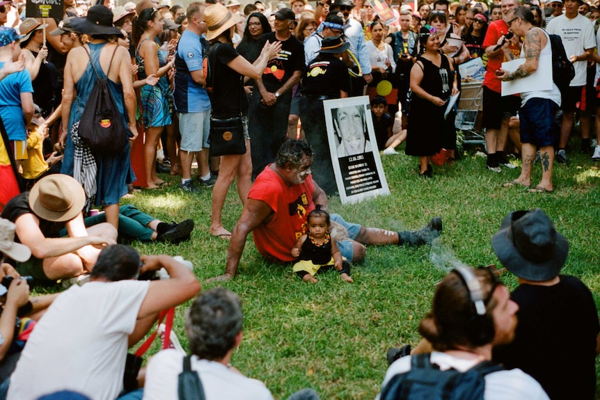 A man sits in the middle of a circle with a child at Yabun Festival, 2019.