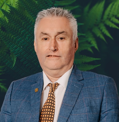 Mike Mehigan, with white hair, wearing a blue suit, looks at the camera.