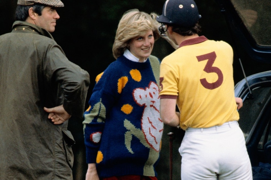 Woman wearing colourful jumper with a koala motif on front talking to man in polo uniform.