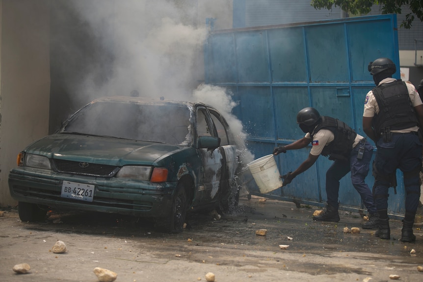 un policier jette de l'eau sur une voiture en feu lors d'une manifestation en Haïti