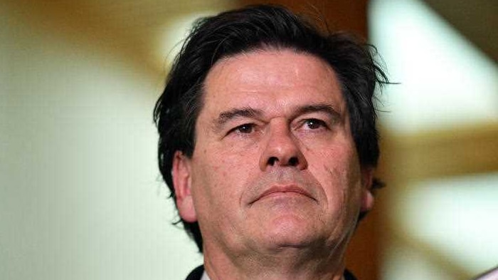 Man with black hair and wearing a suit speaks to reporters in Parliament House, Canberra.