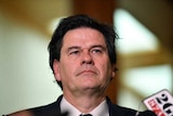 Man with black hair and wearing a suit speaks to reporters in Parliament House, Canberra.