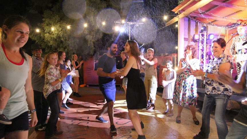 Two people dance surrounded by a crowd as it rains.
