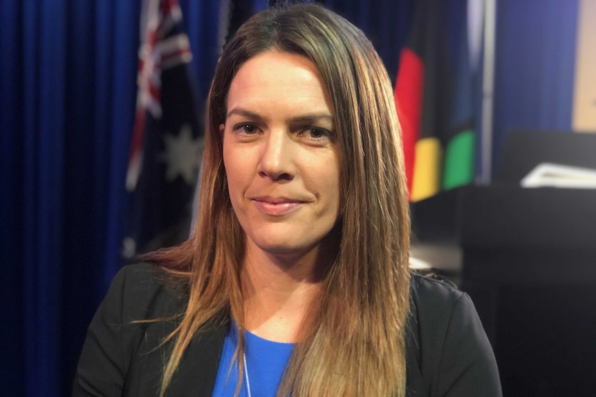 Portrait of a woman with straight brown hair with a blue curtain and flags out of focus in the background.