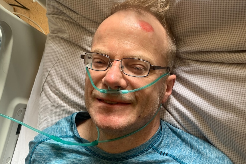 Richard in a hospital bed, oxygen tubes on his face, a big red bump on his forehead.