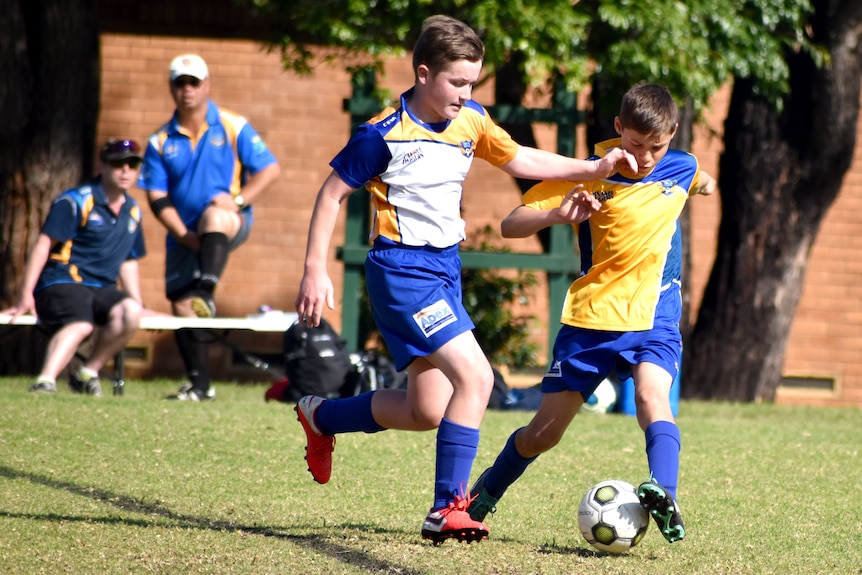 A boy runs with the ball in a soccer game as an opponent closes in and gets ready to tackle.
