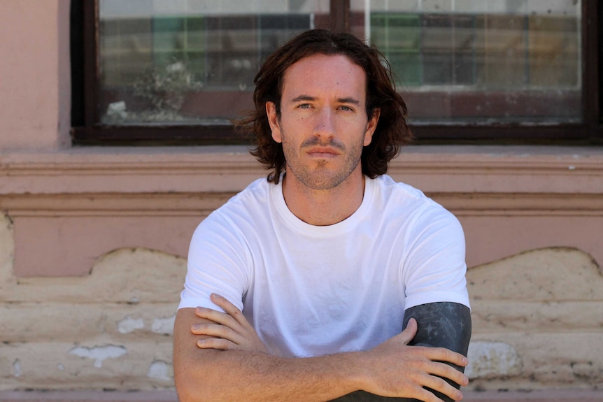 Man in white t-shirt with arms crossed looking at the camera.