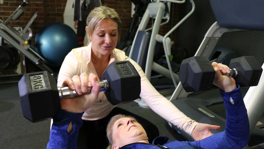 Personal trainer Kylie Willey helps a client lift weights.
