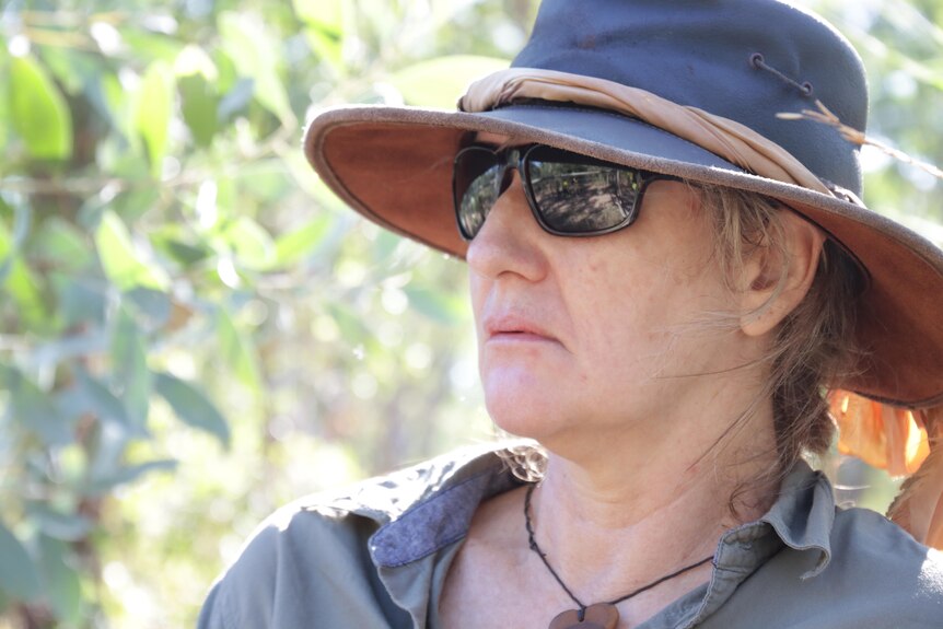 a woman wearing a broad-brimmed hat and sunglasses in the bush
