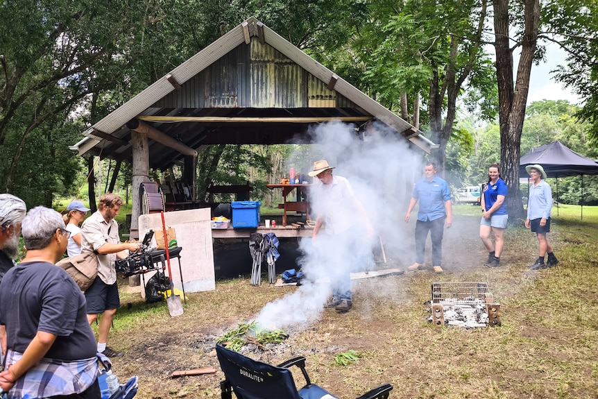 A smoking ceremony takes place at an outdoor camp.