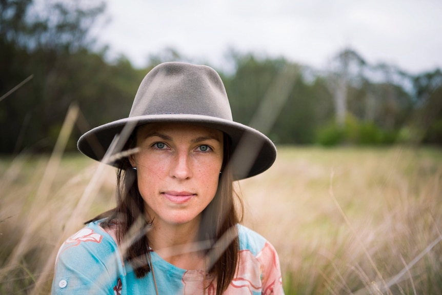 portrait of young woman wearing a hat sitting in a field of long grass