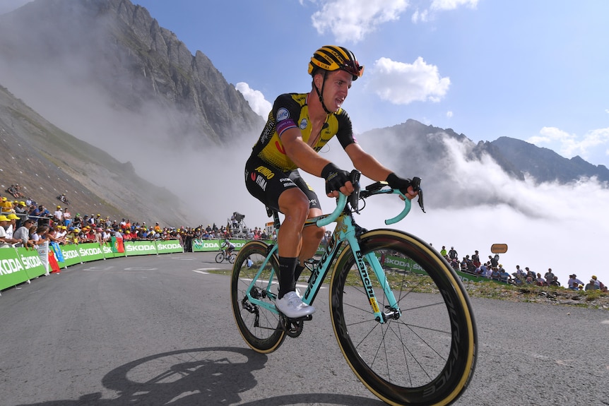 A road cyclist rides up a mountain with clouds in the background