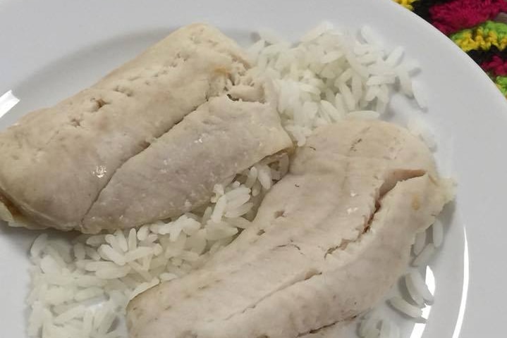 Two pieces of cooked fish sitting on top of white rice on a plate.