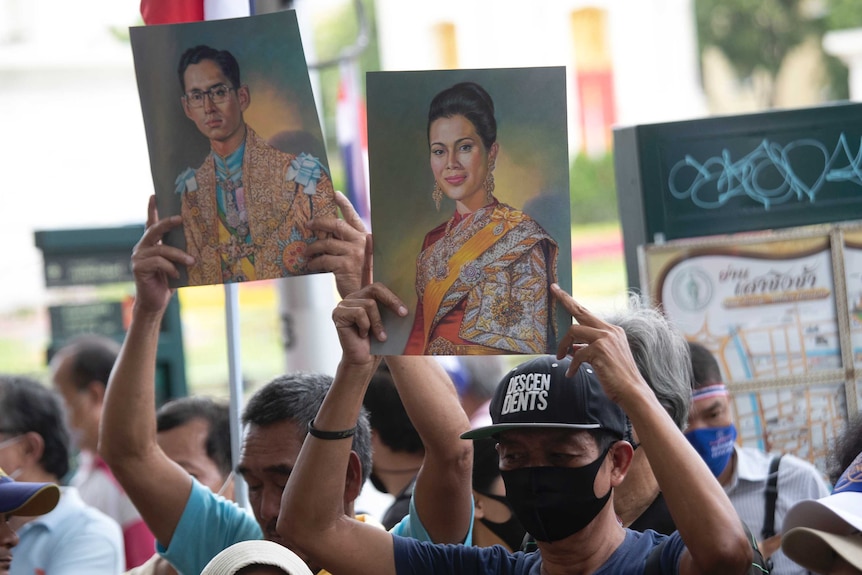 Counter protester hold up pictures of two members of the royal family in formal dress.