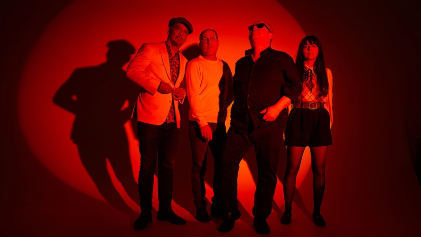 Four members of Pixies stand in a completely re-lit room. Three members look to camera, Frank Black looks up, wearing sunglasses