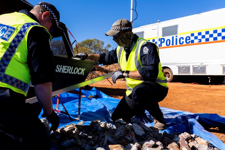 Police sift through rubble on giant tarps in an outback setting
