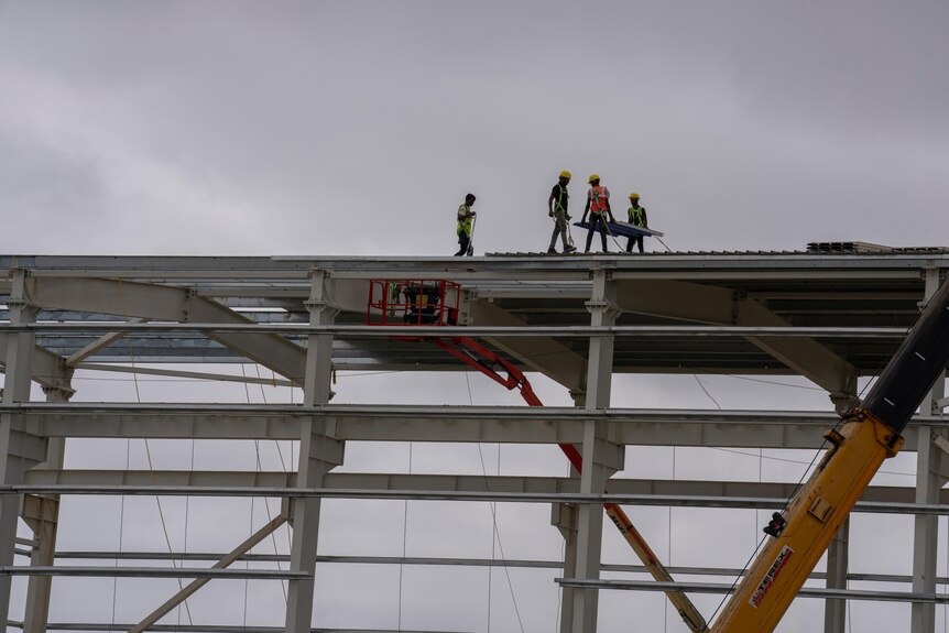 Workers walking across high panel on construction site.
