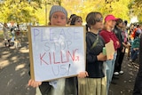 A young woman holds up a sign that says  please stop killing us