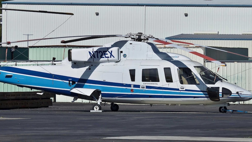 A helicopter, stationary, on the tarmac at an airport