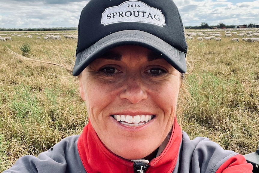 A woman wearing a cap smiles in front of a flooded paddock