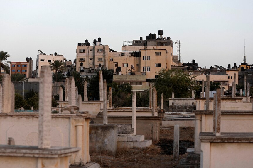 View from a cemetery. Through the graves damaged apartment buildings are up on a hill. 