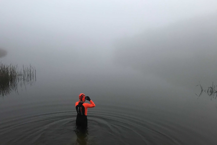 person in wetsuit swimming in cold, foggy water.
