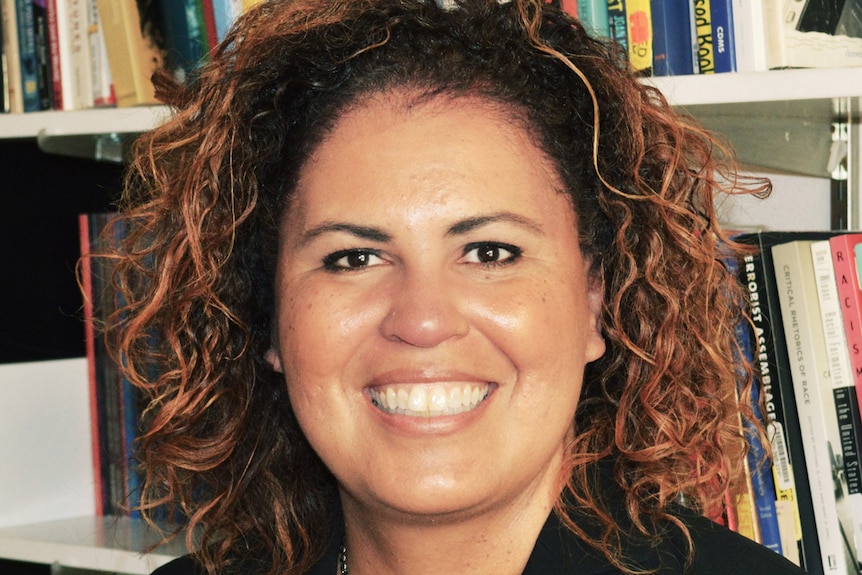 Safiya Noble, standing in front of a bookshelf, smiles at the camera.